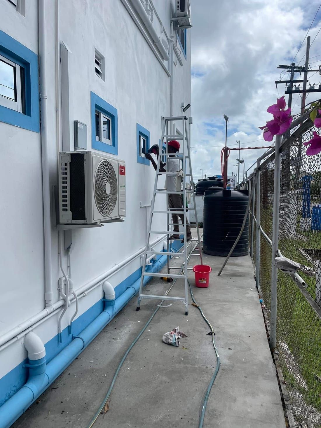 A CDCS worker on a ladder cleaning the exterior windows of a two-storey commercial building