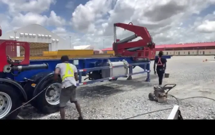 Two CDCS workers in high-visibility vests washing a trailer and lifting equipment at an industrial yard in Guyana