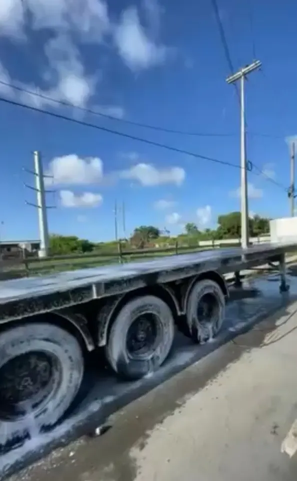 Cleaning foam on the wheels and deck of a flatbed trailer during a CDCS fleet wash in Guyana