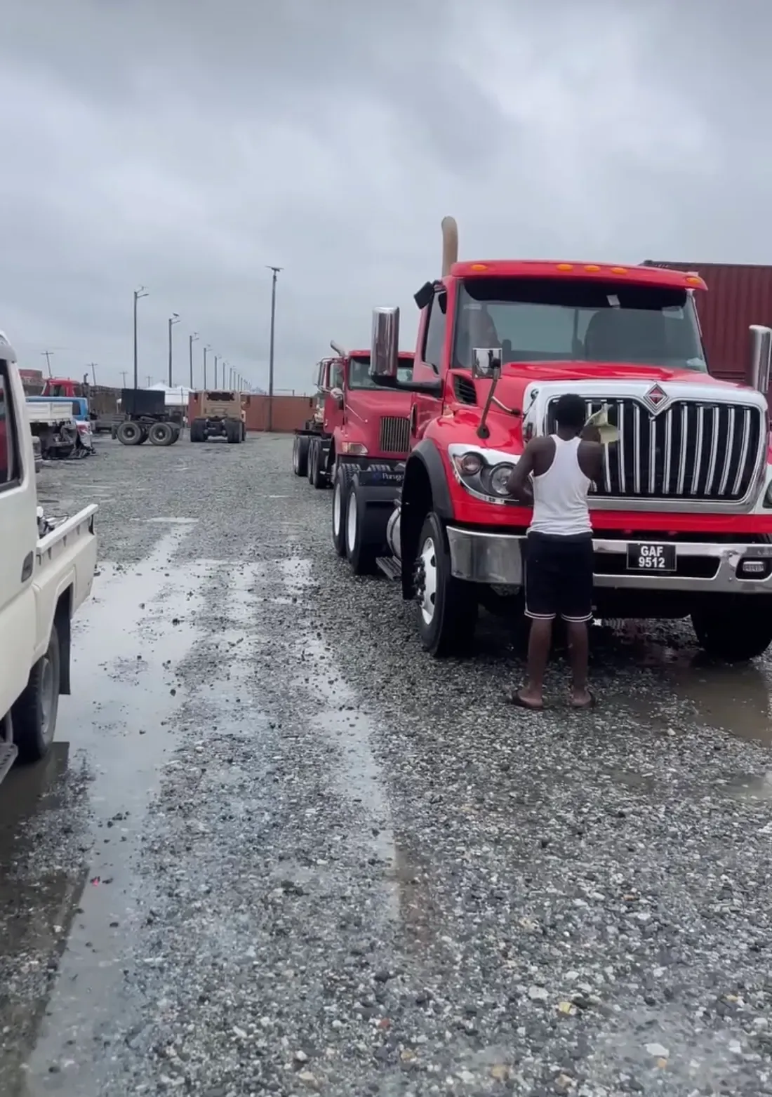 A CDCS worker cleaning the front of a commercial truck at a fleet yard in Guyana