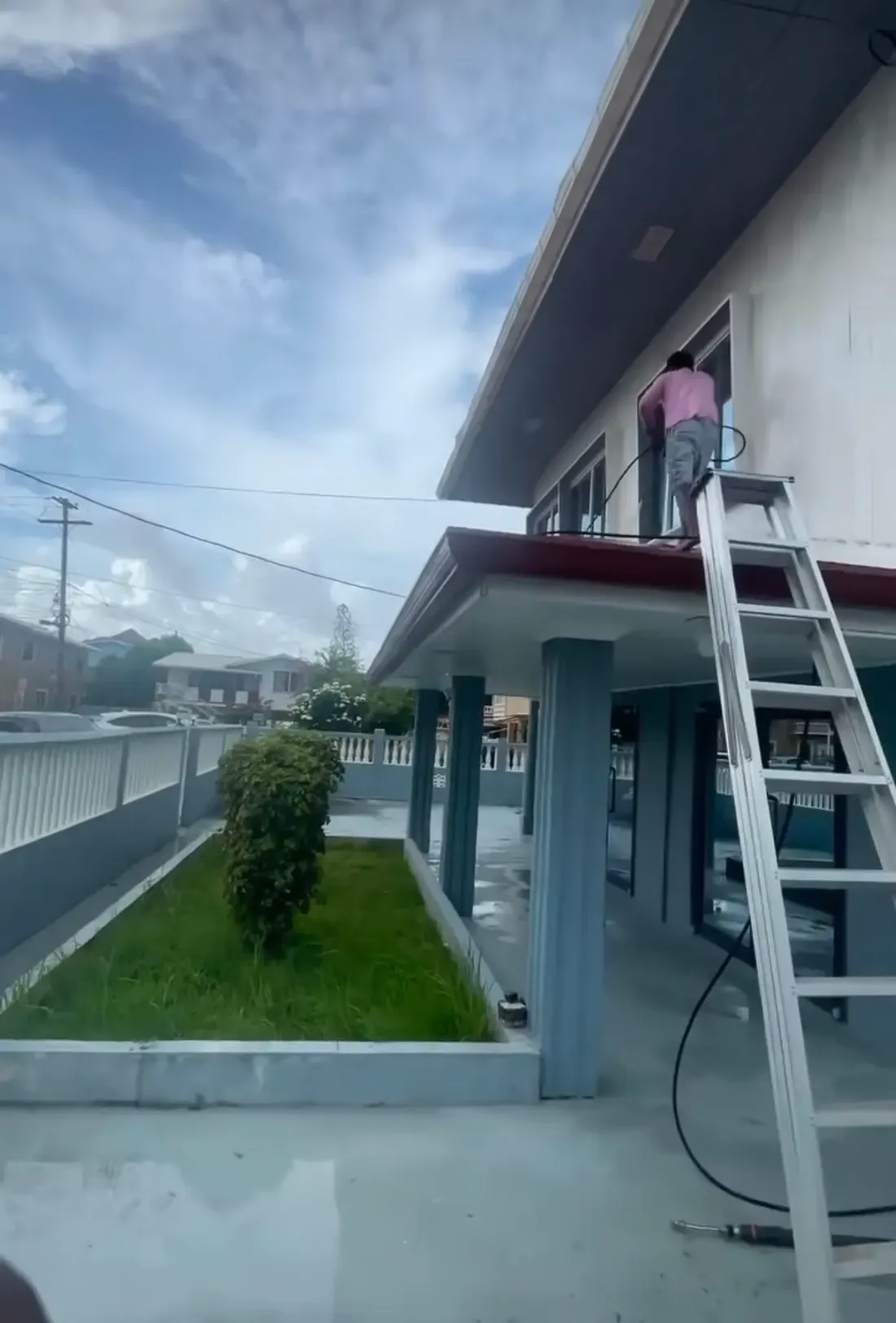 A CDCS worker on a ladder pressure washing the exterior wall and windows of a building