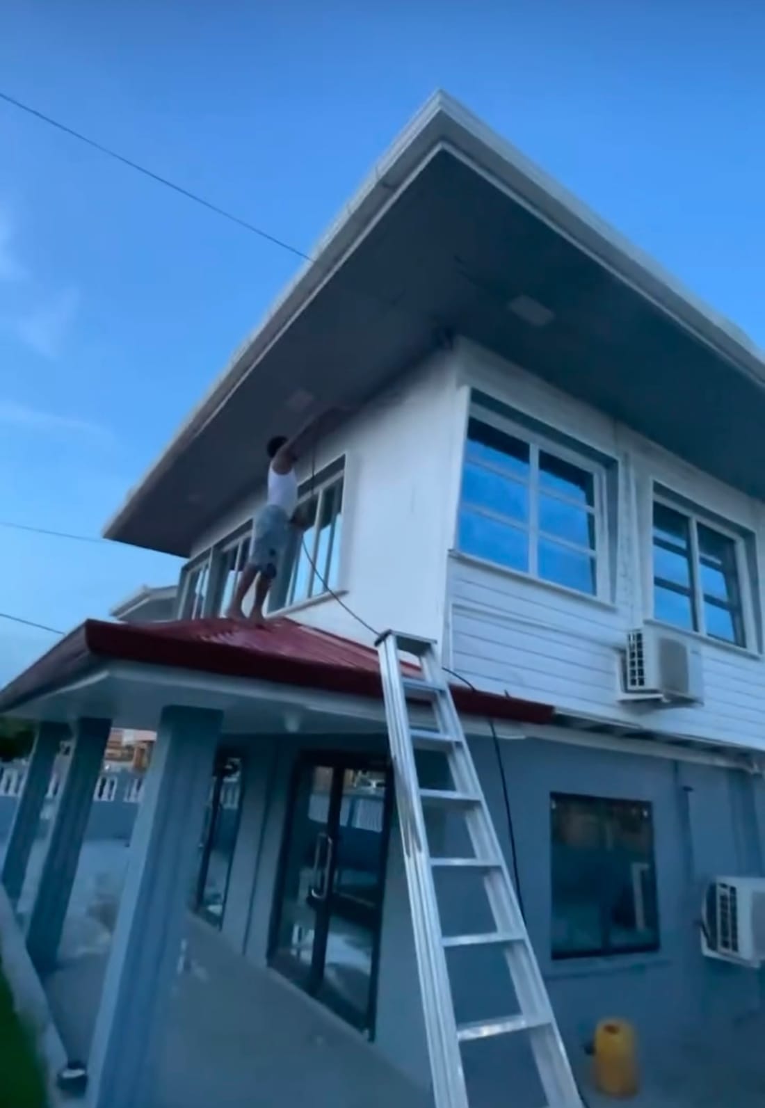 A CDCS worker pressure washing the exterior of a two-storey commercial building in Guyana at dusk
