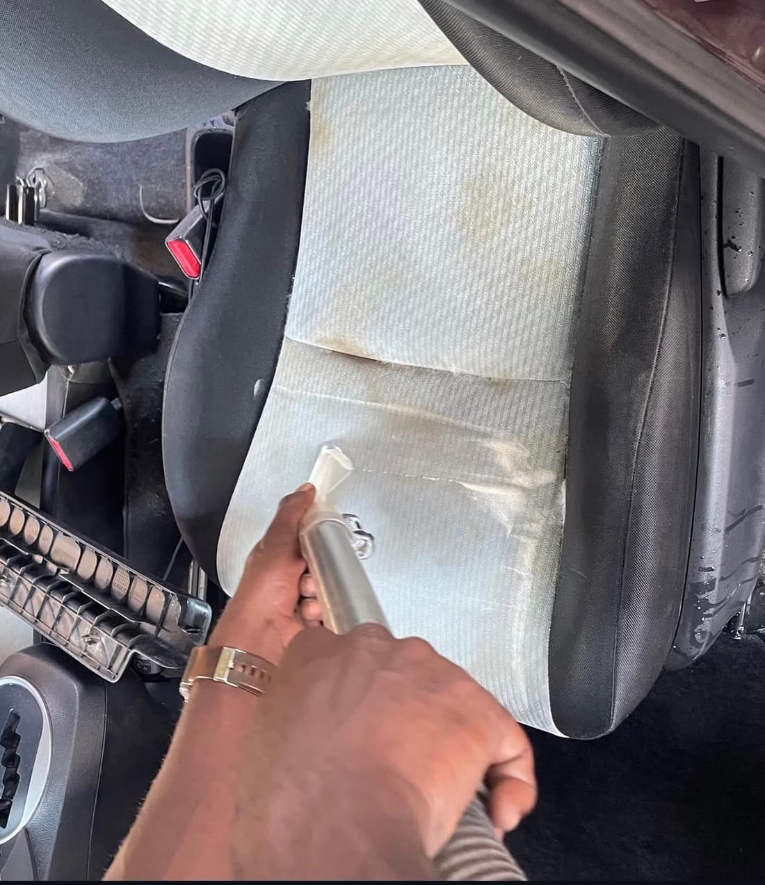 A CDCS worker running a hot-water extraction cleaning tool over a car seat in Guyana, with a cleaned band showing on the fabric